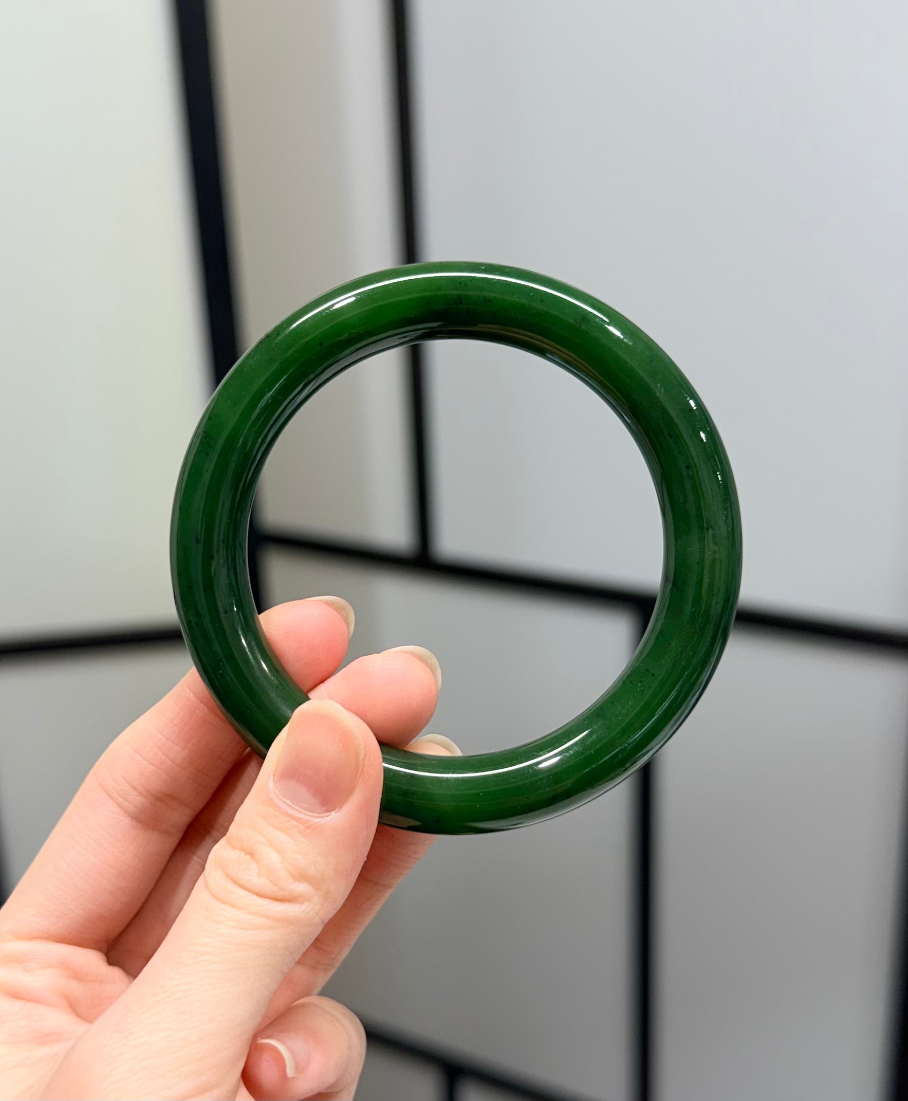 Hand holding a round green jade bangle against a tiled wall background