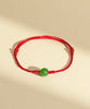 Totally hand-made Red string bracelet with a green natural jade bead on a beige background