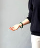 Person wearing a dark sweater and white pants with a green jade bracelet on a plain background