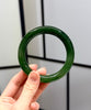 Hand holding a green jade bangle bracelet against a neutral background
