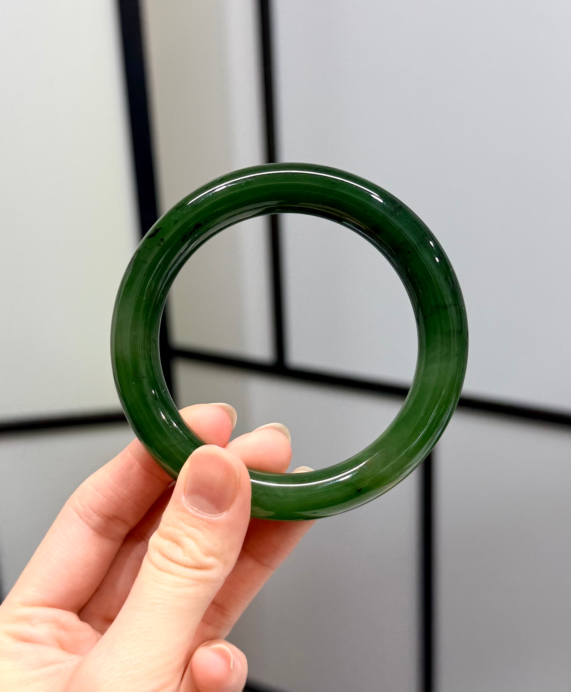 Hand holding a green jade bangle bracelet against a neutral background