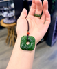 Hand holding a green square pendant with a blurred indoor background