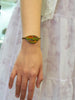 Orange and green ammolite bracelet worn on the wrist alongside a pale lavender dress.