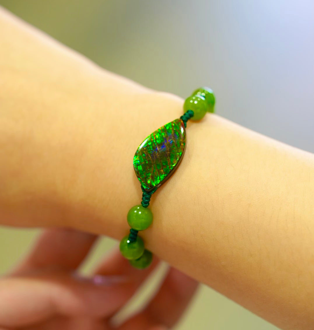 Close-up of an ammolite bracelet on the wrist, highlighting the gemstone’s green and blue colour patterns and green beads.