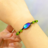 Close-up of a genuine Canadian ammolite doublet bracelet featuring an iridescent green and blue gemstone, worn on an adjustable wristband with green accent beads.