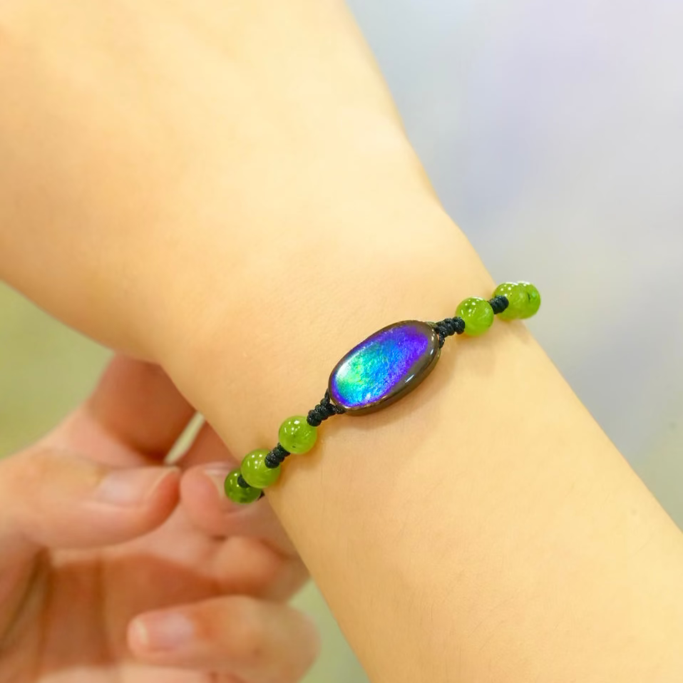 Close-up of a genuine Canadian ammolite doublet bracelet featuring an iridescent green and blue gemstone, worn on an adjustable wristband with green accent beads.