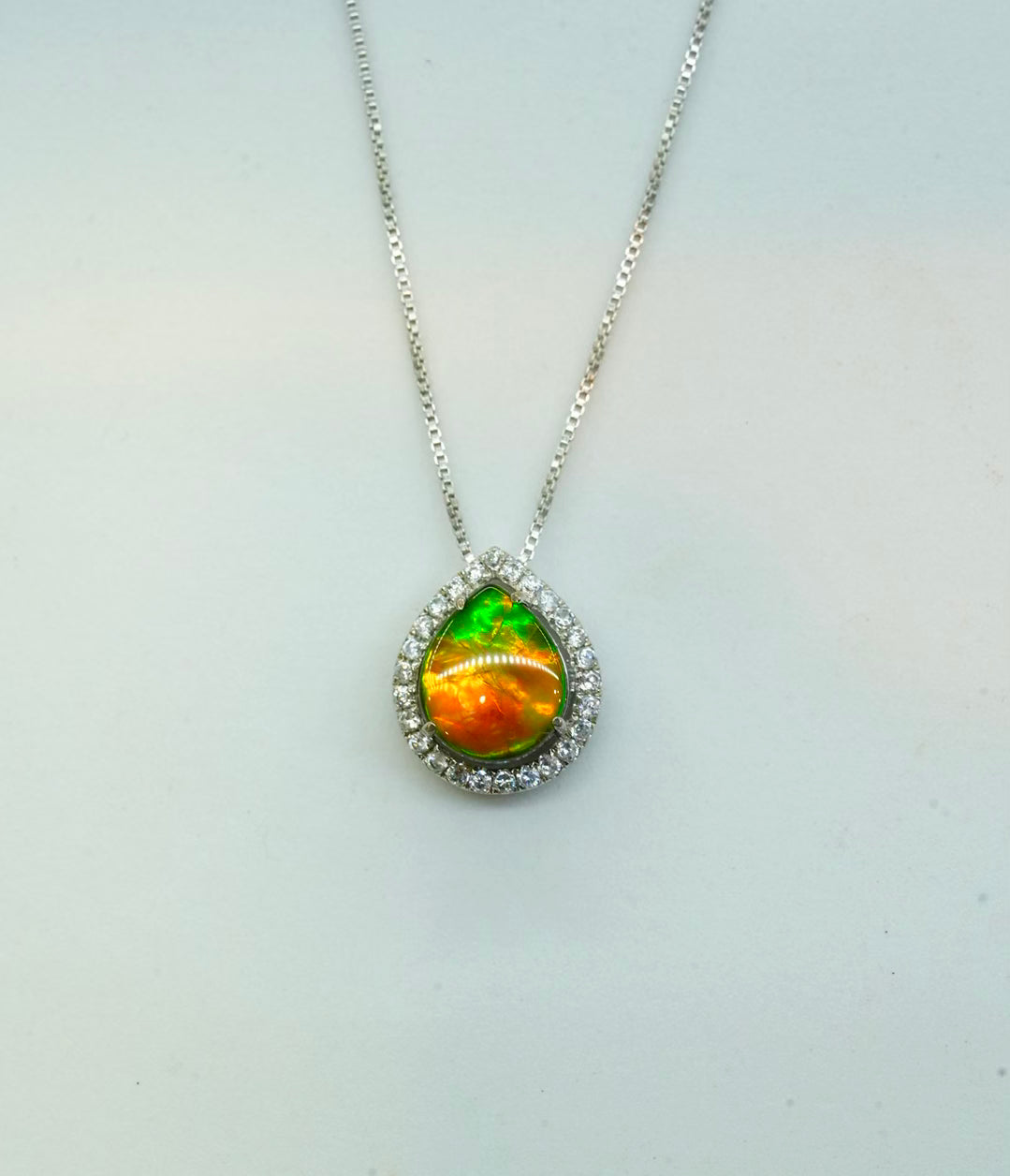 Handcrafted Canadian Ammolite waterdrop pendant featuring an iridescent green and orange gemstone set in 925 sterling silver with a box chain