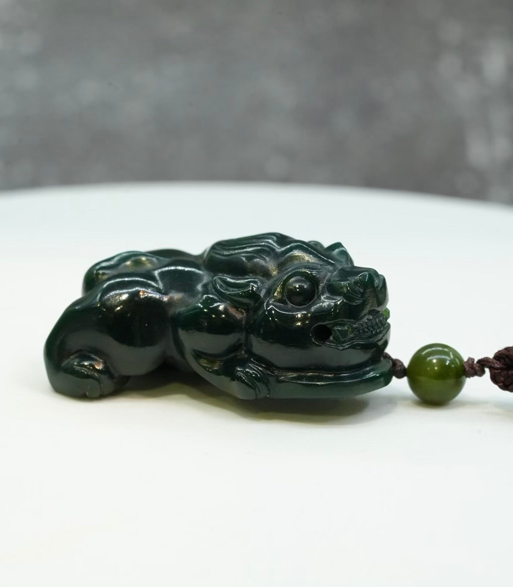 Hand-carved Canadian Polar Nephrite Jade Pixiu pendant resting on a surface, featuring deep spinach green color, intricate details, and a matching jade bead #2441.