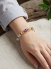 A model wearing the natural multi-gem crystal bracelet on her wrist, showcasing the 10mm Golden Rutilated Quartz and Canadian Polar Jade beads against a linen fabric background.