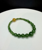 Green arctic nephrite jade beaded bracelet with descending bead sizes and a single gold rutilated quartz crystal bead on a white background.