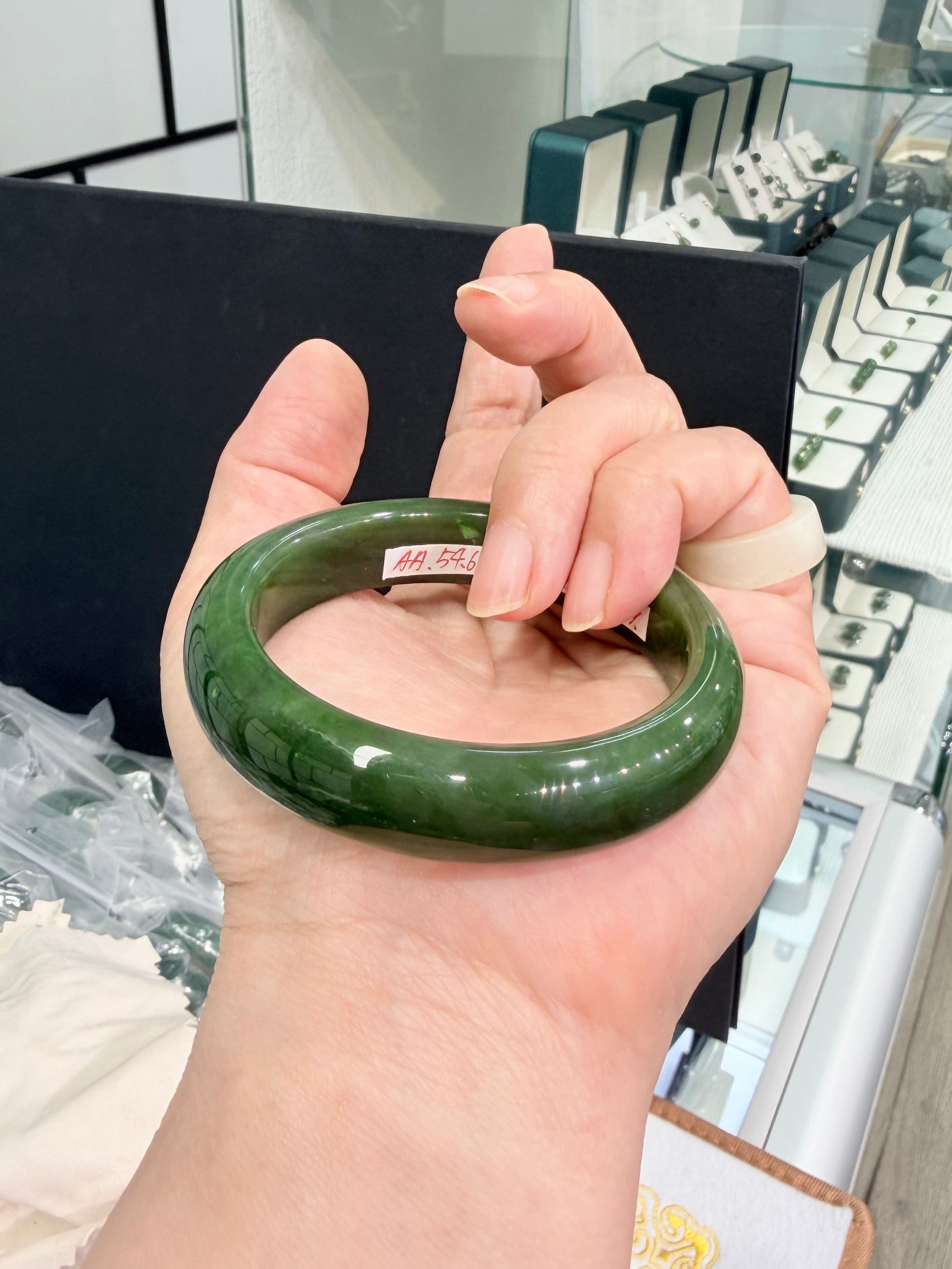 Hand holding a green nephrite Jade bracelet bangle with a jewelry store in the background