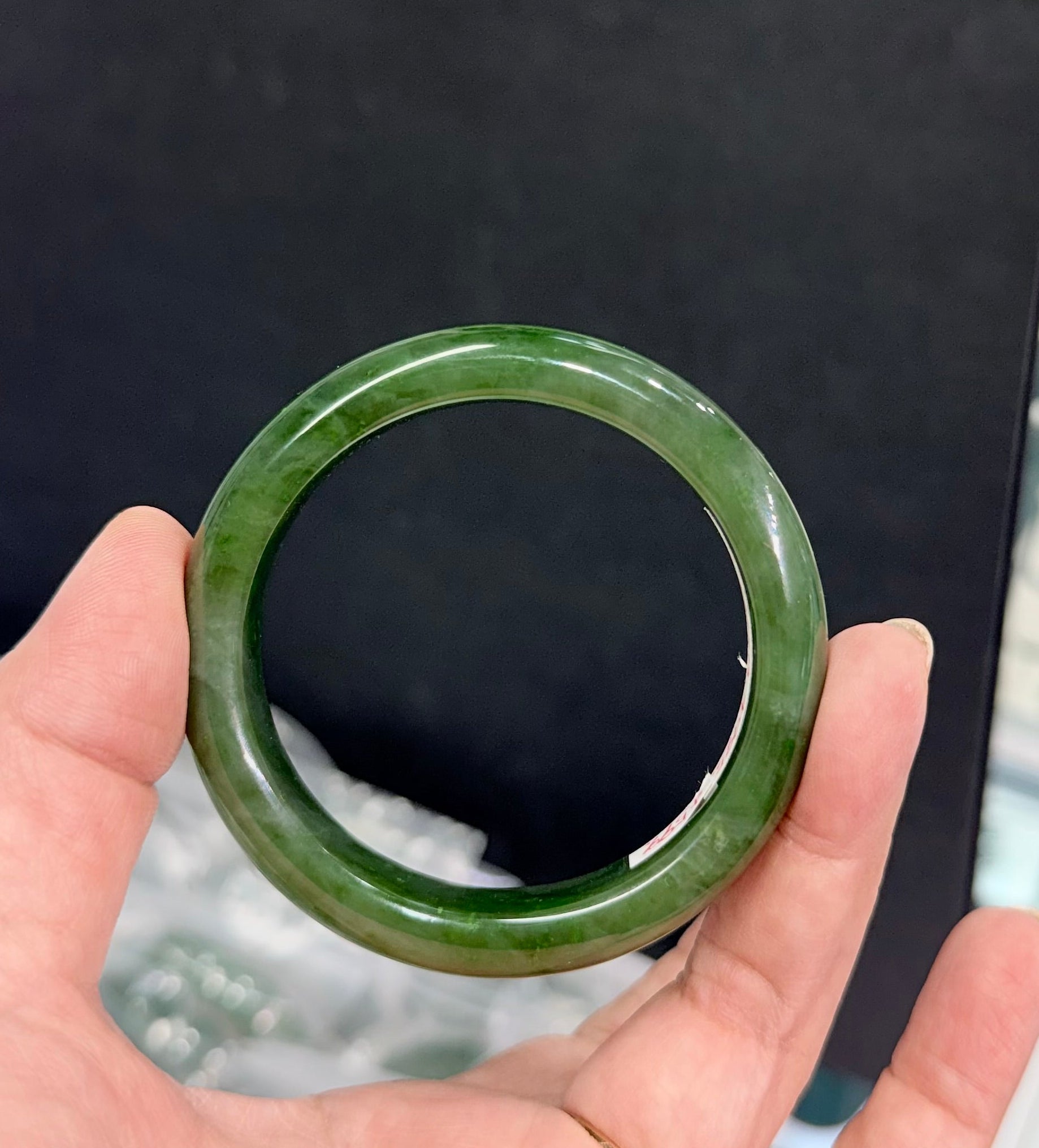 Hand holding a green nephrite jade bracelet bangle against a blurred background
