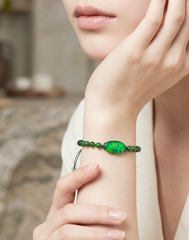 A person wearing a handcrafted beaded bracelet made of green Canadian Polar Jade and an iridescent genuine Ammolite doublet gemstone on her wrist.
